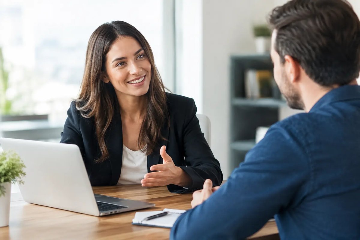 Media sales account executive smiling and explaining campaign results to an advertiser across a desk with a laptop